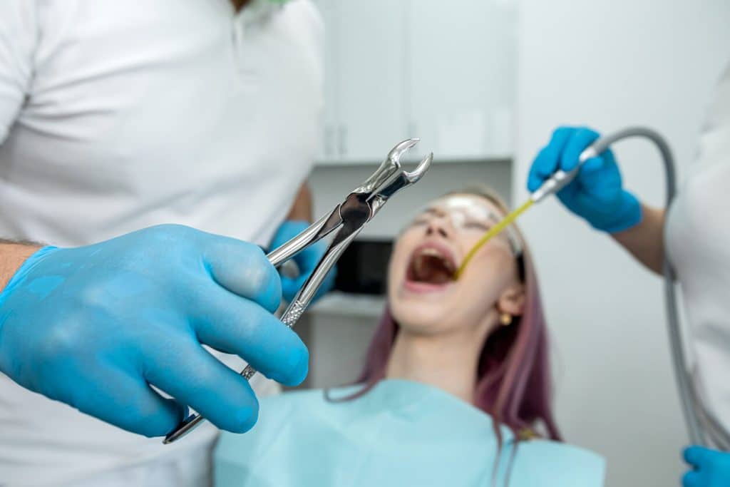 Woman has her tooth extraction treated by male dentist female assistant during an appointment